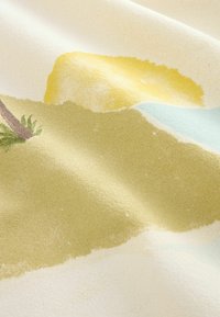 Tissu doux avec des formes abstraites pastel en jaune, vert, bleu et marron, montrant la texture et des plis doux.