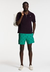 Dark purple short-sleeve polo shirt with a soft texture, paired with green swim shorts featuring a bird pattern and white sneakers.