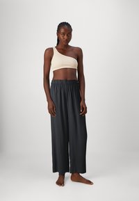 Top corto de punto en color beige con un solo hombro, combinado con pantalones de pierna ancha negros. El top presenta un diseño texturizado y los pantalones tienen una cintura elástica.