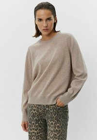 Puloverură tricotat bej cu guler rotund și mâneci lungi, asociat cu pantaloni cu imprimeu leopard, care au o croială lejeră și buzunare.