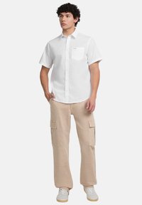 Witte short-sleeve button-up shirt met een borstzak, gecombineerd met beige cargo broek met zijzakken, gedragen met witte sneakers.