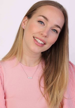 Zilveren ketting met drie ronde, heldere edelstenen. Model die een geribbelde roze top draagt met gekruiste mouwen en lang, steil haar.