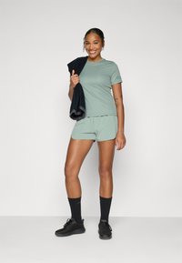 Light green athletic shirt and shorts, black sports shoes, and dark towel. The fabric appears smooth; the design is simple with a relaxed fit.