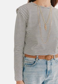 Langærmet, stribet top i cremet og marineblå, med en rund halsudskæring. Kombineret med lyseblå jeans og et lysebrunt, vævet bælte med en cirkulær spænde.
