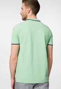 Zielona koszulka polo z kontrastującym granatowym paskiem przy mankietach, krótkimi rękawami i klasycznym kołnierzykiem. Wykonana z miękkiego bawełnianego materiału.