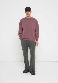 Bordeauxfarbiges Sweatshirt mit rundem Ausschnitt und überschnittenen Schultern, kombiniert mit enganliegenden grauen Sweatpants und schwarzen Sneakers.