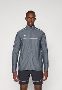 Gray zip-up athletic jacket with white accents and long sleeves, made of a smooth, moisture-wicking material. Worn over dark shorts.