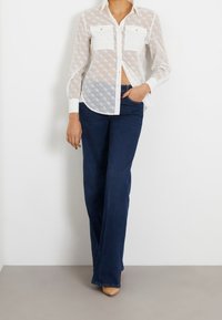 White sheer button-up shirt with diamond pattern and two chest pockets, paired with dark blue flared jeans and nude heels.