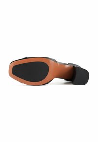 Zwarte hak schoen met een gladde afwerking, voorzien van een oranje rubberen zool en een gestructureerde zwarte hak, ontworpen voor stabiliteit en grip.