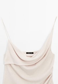 Cowl-neck top in lichtbeige stof met dunne bandjes en een zachte textuur. Voorzien van een label met "Massimo Dutti" bij de hals.