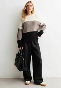 Pull en tricot beige, crème et noir ; présente une coupe décontractée, une texture côtelée et des manches longues. Assorti à un pantalon large noir et un sac à main.