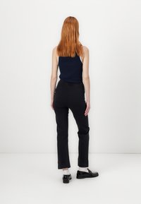 Mornarsko modra brezrokavnik v kombinaciji s črnimi slim-fit hlačami z teksturirano obdelavo in manšetami. Model nosi črne �čevlje in bele nogavice.