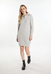 Grijze geribbelde gebreide jurk met een kwart-rits halslijn, lange mouwen en een korte zoom, gecombineerd met zwarte enkelboots. Minimale branding op de zoom.