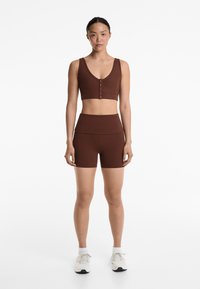 Brown activewear set featuring a ribbed cropped tank with buttons and high-waisted shorts. Smooth texture, fitted design, minimalistic style.