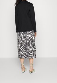Blazer nero su misura, gonna al ginocchio con strisce zebrate in bianco e nero, e tacchi a strappo verde menta. Tessuto liscio con una leggera lucentezza.