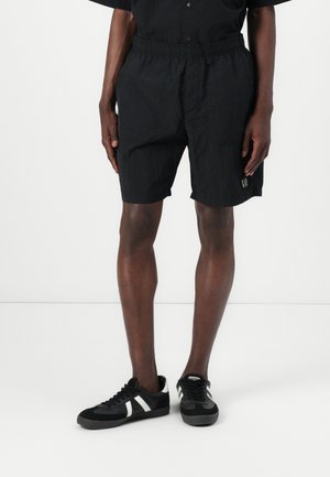 Black, lightweight shorts with an elastic waistband and side pockets, featuring a subtle logo detail on the hem. Paired with black sneakers.