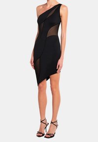 Svart enaxlad klänning med genomskinliga paneler, asymmetrisk nederkant och figursydd design. Matchad med svarta högklackade sandaler med remmar.