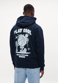 Hanorac bleumarin dintr-un amestec de bumbac, cu o croială lejeră. Dispune de un imprimat grafic mare pe spate, textul "PLAY COOL" și mansete ribbate.