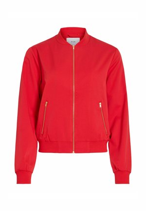 Sarkana bumbvedera virsjaka ar priekšējo rāvējslēdzēja aizdari, divām sānu kabatām ar rāvējslēdzējiem, ribota apkakle, aproces un apakšmala, zīmola etiķete apkakles iekšpusē.