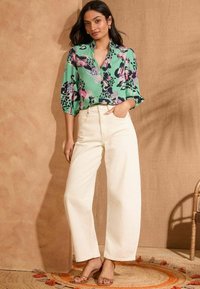 Gėlių raštų žalia palaidinė su trijų ketvirčių rankovėmis, derinama su aukštu liemeniu, plačiomis, kreminio atspalvio kelnėmis. Užsidėta su rudos spalvos diržinėmis basutėmis.