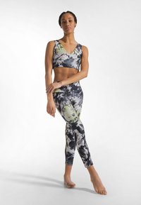 Sujetador deportivo y leggings con un patrón tie-dye en negro, blanco y verde. La tela es elástica, ajustada y suave, con un diseño de escote en V en la parte superior.