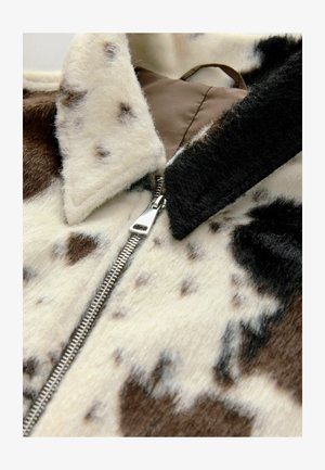 Faux fur jacket featuring a cream and brown cow print, with a silver zipper and black collar, highlighting soft texture and varying patterns.