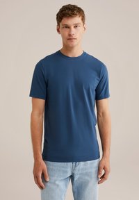 Tricou din bumbac de culoare bleumarin, cu mâneci scurte, guler rotund și siluetă ajustată, asociat cu blugi de culoare albastru deschis.