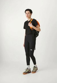 Mustmustern must t-särgid, mustad retuusid, millel on valge logo, hallid ja oranžid matkasaapad ning oranžiga kaunistatud seljakott.