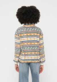 Karvane pullover kõrge kraega. Mitmevärvilised geomeetrilised mustrid oranži, sinise, rohelise ja valgega. Soonikkoes mansetid. Pehme tekstuur.