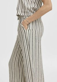 Pantalons larges à rayures en tissu beige et gris foncé, dotés d'une taille élastique, de poches latérales et d'une coupe ample.