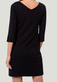 Robe noire avec un décolleté en V et des manches trois-quarts. Présente des accents cloutés sur les ourlets des manches, fabriquée à partir d'un tissu texturé.