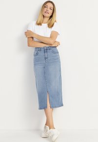 Ljusblå denimkjol med en framslits, hög midja och fem fickor, kombinerad med en vit kortärmad skjorta och vita sneakers.