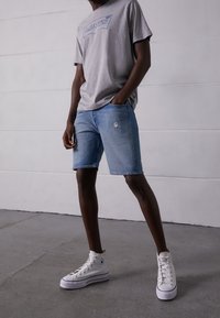 Grå bomullströja med blå Levi's-logga, tillsammans med ljusblå denimshorts med en sliten detalj, kompletterat med vita högskurna sneakers.