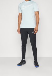 Light blue short-sleeve Nike shirt with logo; paired with black tapered pants featuring a white logo. Black and blue athletic shoes.