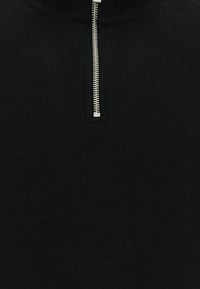 Jersey negro con cuello corto con cremallera; hecho de tela suave. Cuenta con cuello acanalado y un pequeño logo en el lado izquierdo.