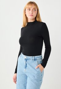 Czarna bluzka z długim rękawem i wysokim kołnierzem, zestawiona z jasnoniebieskimi, wysokim stanem dżinsami. Miękka tekstura, dopasowany krój, minimalistyczny styl.