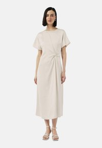 Sukienka do kolan w kolorze kremowym, z okrągłym dekoltem i krótkimi rękawami. Posiada skręcony detal w talii i gładką fakturę.