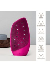 Dispositif de lavage facial en silicone rose vif avec surface texturée, forme ergonomique et commandes par bouton. Étanchéité de niveau IPX7.
