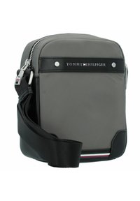 Borsa a tracolla grigia in nylon con dettagli in pelle nera, zip argentata, tracolla regolabile e logo "TOMMY HILFIGER" sul davanti.