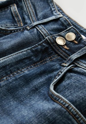 Mørkeblå denimjeans med kobberfarvede metalknapper, markante søm og en let falmet tekstur på stoffet.