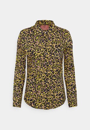 Chemise à manches longues boutonnée avec un motif floral abstrait multicolore en jaune, rose et noir sur fond blanc.