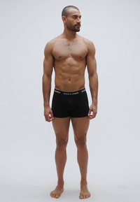 Svarta bomullsboxershorts med ett mjukt elastiskt midjeband med "JACK & JONES"-logotyp. Modellen har en muskulös kroppsbyggnad och är barfota.