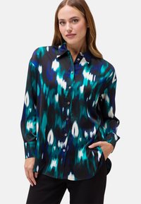 Camicia button-up in un vivace pattern astratto blu-verde e nero, con maniche lunghe e una superficie di tessuto liscia e lucida.