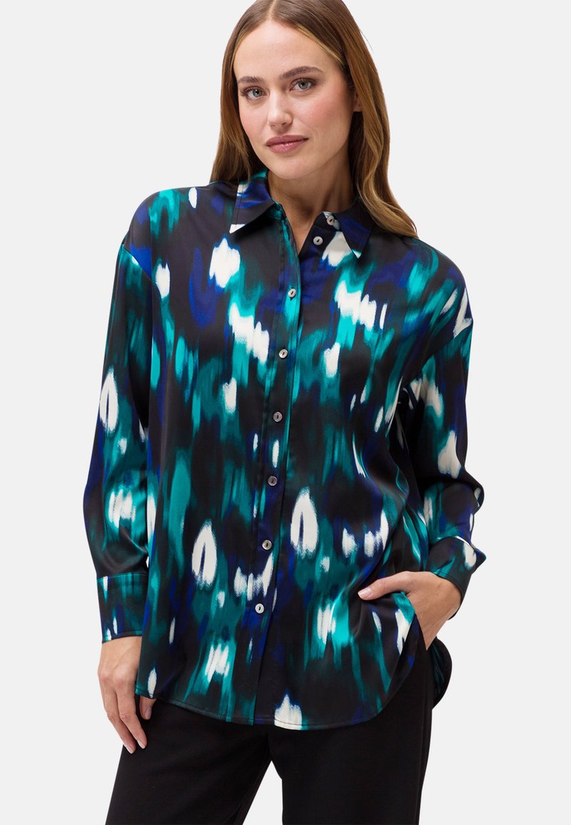 Camicia button-up in un vivace pattern astratto blu-verde e nero, con maniche lunghe e una superficie di tessuto liscia e lucida.