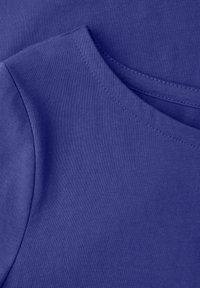 Nærbillede af en foldet blå bomulds-T-shirt, der viser halsudskæringen og sømmen på ærmet med synlige stingdetaljer.