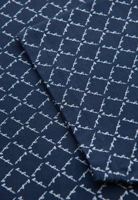 Námořnická látka s diamantovým vzorem a bílým ručně psaným textem. Materiál vypadá měkce s texturovaným povrchem.