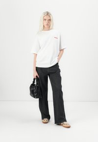 White oversized t-shirt with red text, paired with black wide-leg jeans. Accessorized with a black bag and light-colored sneakers.