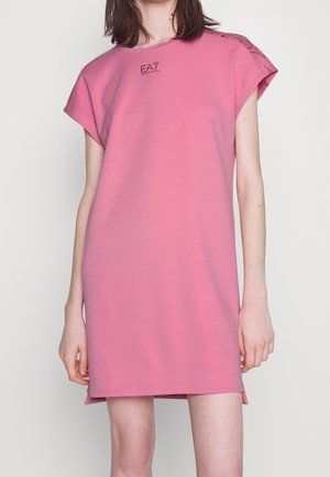 Kobieta nosząca luźną, sięgającą kolan różową sukienkę z krótkimi rękawami i małym logo "EA7 Emporio Armani" na górnej części klatki piersiowej.