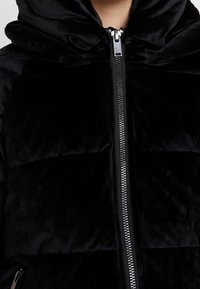 Czarna kurtka puchowa z aksamitu, charakteryzująca się miękką, wyściełaną strukturą, wysokim kołnierzem oraz przednim zamkiem błyskawicznym z metalowymi detalami.