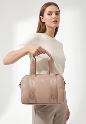 Femme portant un haut beige et un pantalon tient un sac à main en cuir taupe avec de larges anses griffées "DIANA&CO."